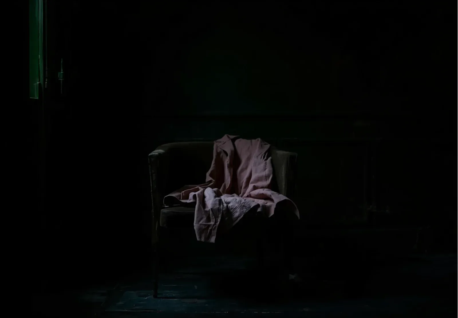 An empty armchair draped with a mauve shirt in a dark room